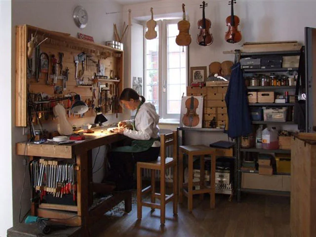 Instrumentenbouwer aan de werkbank in een atelier met gereedschapswand en hangende instrumenten